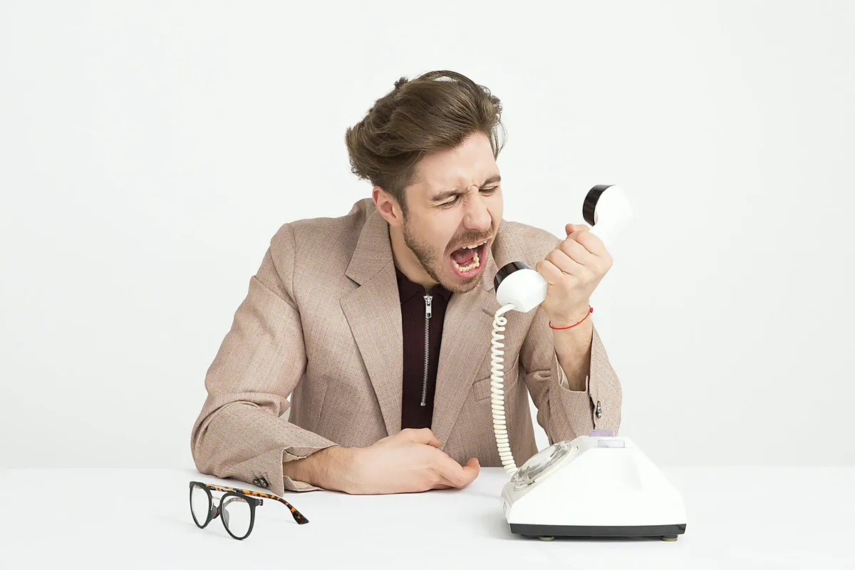 Frustrated man yelling into a phone, showing the consequences of poor contact center outsourcing services and lack of customer support quality.